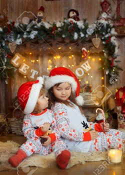86474131 happy little sisters in pajamas playing near a fireplace at christmas eve